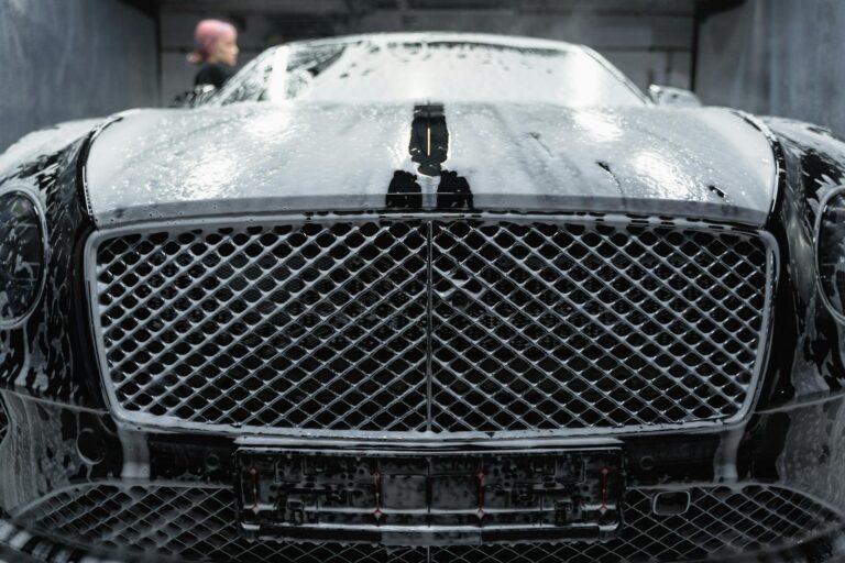 A close-up of a luxurious black car being cleaned with foamy soap at a carwash.