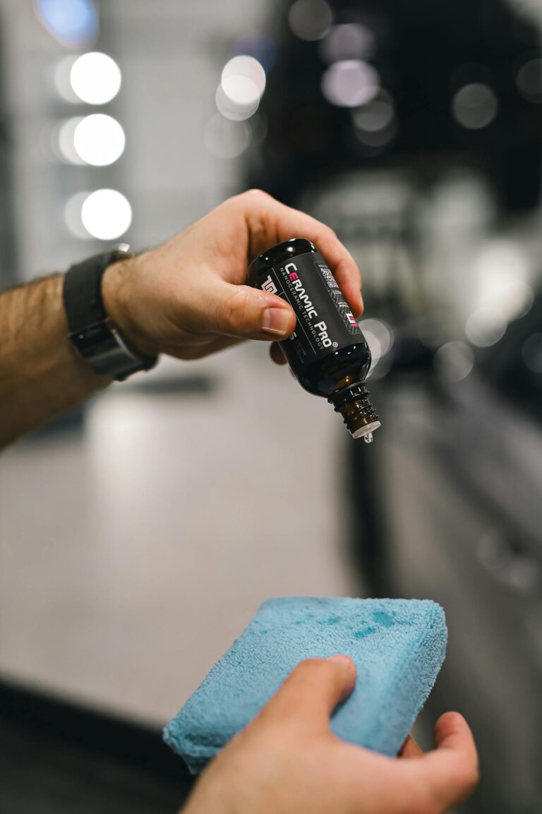 Hands applying car detailing liquid with a blue sponge for a shiny finish.